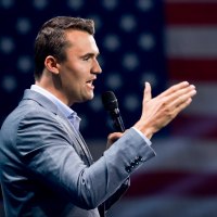 Charlie Kirk speaks on stage, American flag backdrop