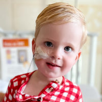 Beckett Wear sits on a hospital bed with a tube entering his nostril taped to his face
