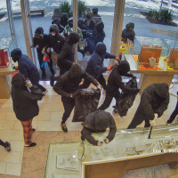 Security footage shows a group of masked and hooded robbers enter a jewelry store and break the glass display while bagging jewelry in black trashbags