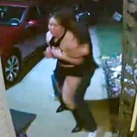 A video footage still of a woman being grabbed and taken by a man in front of a porch outside, in a driveway