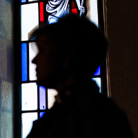 Pastor stands silhouetted by stained glass windows.