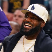 Oct 5, 2025; San Francisco, California, USA;  Los Angeles Lakers forward LeBron James (23), wearing a Los Angeles Dodgers hat, smiles after watching his son, guard Bronny James (9), dunk a rebound against the Golden State Warriors in the third quarter at Chase Center. Mandatory Credit: David Gonzales-Imagn Images