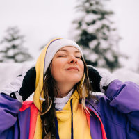 Woman wearing winter clothes enjoying winter snowfall in forest