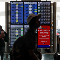 Travelers walk past the flight information display system at Los Angeles International Airport/