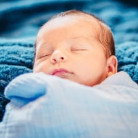 Latinx newborn baby in blue baby blanket.