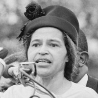Rosa Parks speaks at a podium outside as people stand behind her