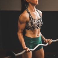 Strong and muscular young woman lifting barbell grip on biceps. Athletic body, girl power.