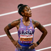 Sha’Carri Richardson gazes upward over her left shoulder while standing with both hands on her hips.