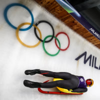 A woman lying back on a luge sled slides past on an ice track.