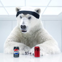 A polar bear looks at a can of Pepsi, left, and a can of Coca-Cola while seated in an all-white room at a table