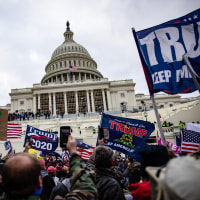 A huge crowd of people waving Trump 2020 flags are gathered outside the U.S. Capitol building under gray skies. 