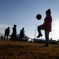 Silhouettes of children playing outside in a field, one bounces a soccer ball up with their knee