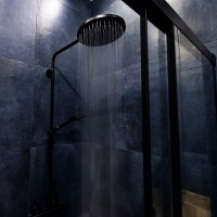 Water running from a black rain shower head in a dark luxury bathroom