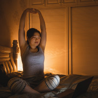asian woman sitting on her bed stretching her back