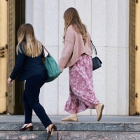 Three women are seen in profile view as they ascend the stone steps to a courthouse.