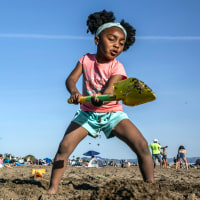 Two girls play with shovels in the sand on a beach during a heat wave.