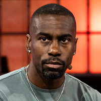 Deray Mckesson sits on a white couch on stage