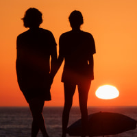 People watch the sunset at Aliso Beach, their silhouettes are seen as they face the water and horizon, orange sky