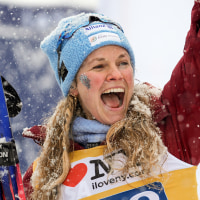 Jessie Diggins smiles while holding two skis in a snowstorm.