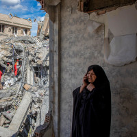 A woman speaks on the phone as emergency workers sift through rubble.