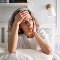 Mature woman lying on bed, expressing negative emotions silently.