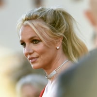 Britney Spears is visible behind a person in soft focus in the foreground.