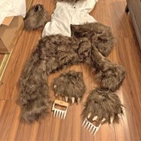 A bear costume and a pair of metal claw-shaped handles lie on a hardwood floor.