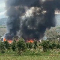 Flames and dark smoke rising from a building in a grassy landscape.