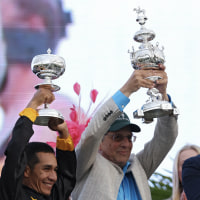 Three men smile while holding silver trophies high into the air.