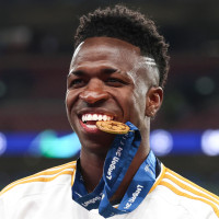 Vinicius Junior bites his winners medal on the soccer field and holds up two fists in celebration