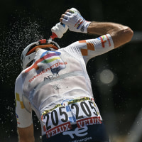 A cyclist pours a bottle of water over his back while riding.