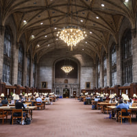 A large stone room with a vaulted ceiling and chandelier and long rows of wooden desks.