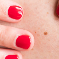Close-up of woman wearing red nail polish touching skin with freckle