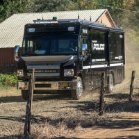 A law enforcement mobile command center driving down a dirt road.