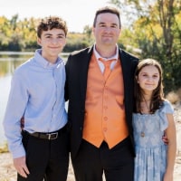 A portrait of a father and two children dressed in formal wear on the banks of a river.