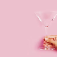 Woman hand holding an empty cocktail glass on a pink background