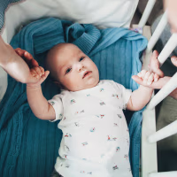 Mother and father holding hands of baby son in crib.