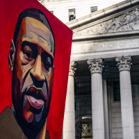 A poster of a painting of George Floyd is held up near a building exterior outside