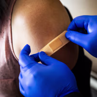 Blue gloved hands place a bandaid on someone's arm