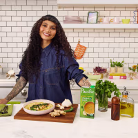 Chef Sophia Roe poses with her Ginger Tea Chicken & Rice with Scallion Sauce recipe and Paific Foods broth on a kitchen counter.
