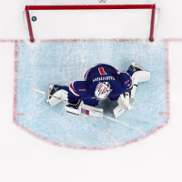 An overhead view of a goalie on the ice, in front of a puck that has drifted past the goal line and into the net.