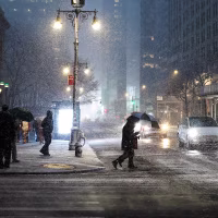 Pedestrians carrying umbrellas navigate heavy snowfall on the streets of Manhattan at night.