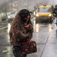 A woman in a short fur coat huddles against the cold as she crosses a street in downtown Manhattan during a snowstorm.