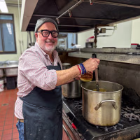 Andrew Zimmern stands beside an oven preparing meals at Soup for You.