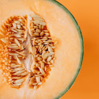 Half of ripe cantaloupe melon with seeds on vibrant orange background, fresh summer fruit concept