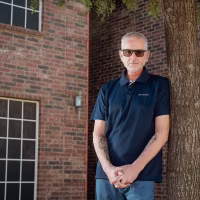 FORT WORTH, TEXAS - FEBRUARY 11, 2026: Guy Shoemaker, 64, poses for a portrait outside his home in Fort Worth, Texas, on Wednesday, Feb. 11, 2026. After his TRICARE plan transitioned to TriWest Healthcare Alliance, tens of thousands of dollars in previously approved claims for life-saving treatment and scans for his throat cancer were pulled back or denied because of a data error.