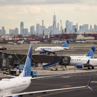Four United Airlines jets sit on a tarmac with the New York City skyline visible in the distance.