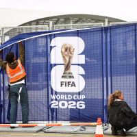 Workers affix FIFA World Cup 2026 logos and signage on a fence outside of SoFi Stadium