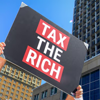 A person holds a sign that reads "TAX THE RICH."