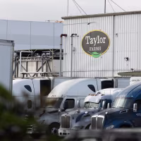 Several semi-trucks parked in front of a warehouse with the Taylor Farms logo on its facade.